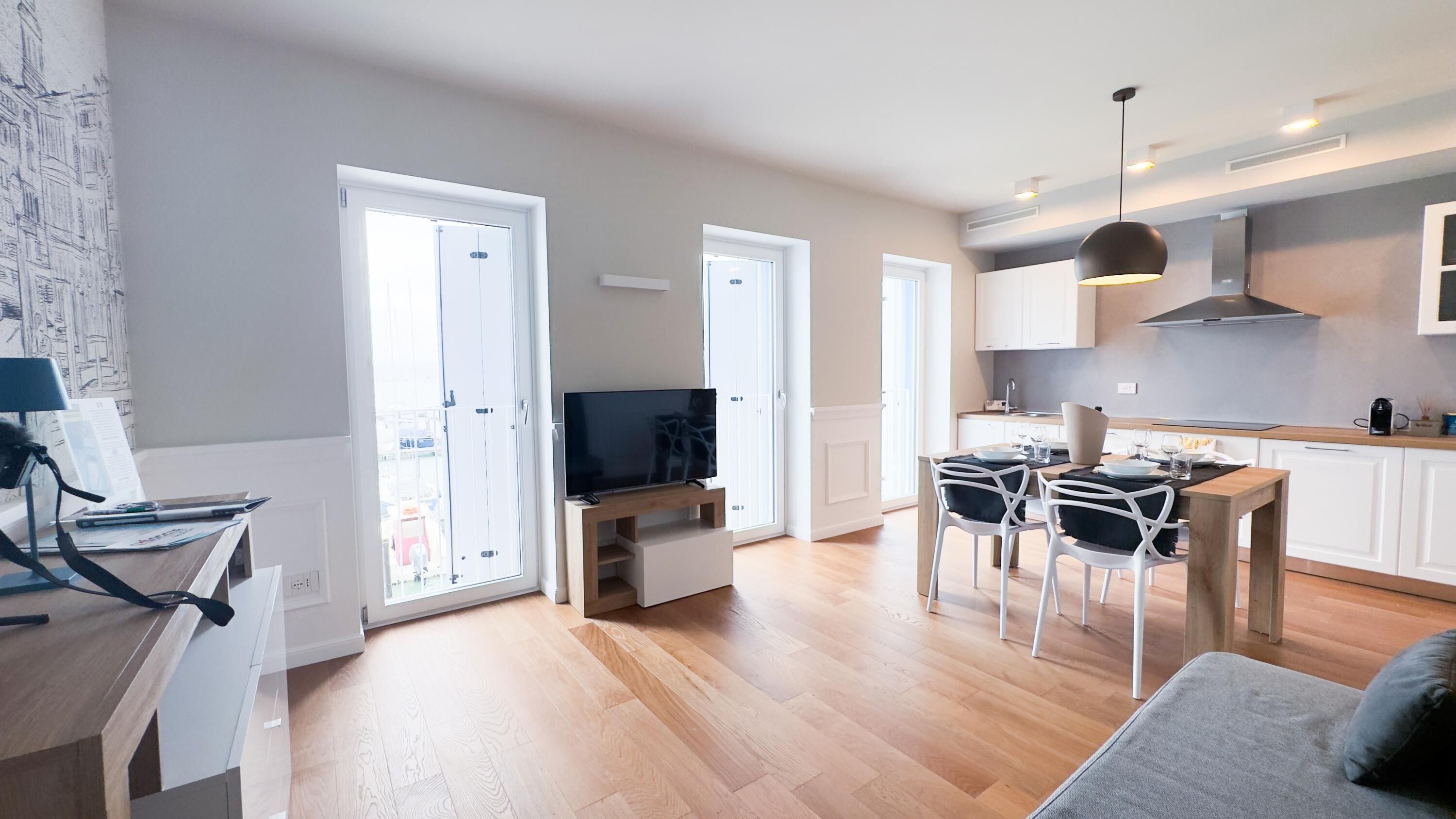 A modern apartment with a dining area, kitchen, and a TV on a stand.