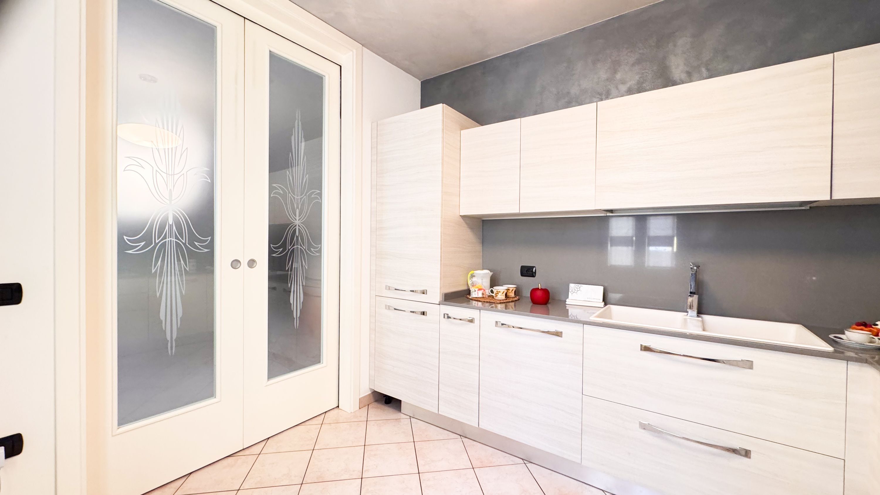 Een moderne keuken met licht houten kastjes, een roestvrijstalen spoelbak en een betegelde vloer.