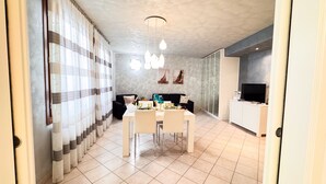 Una sala de estar moderna con comedor, un sofá negro, un televisor y un separador de vidrio.
