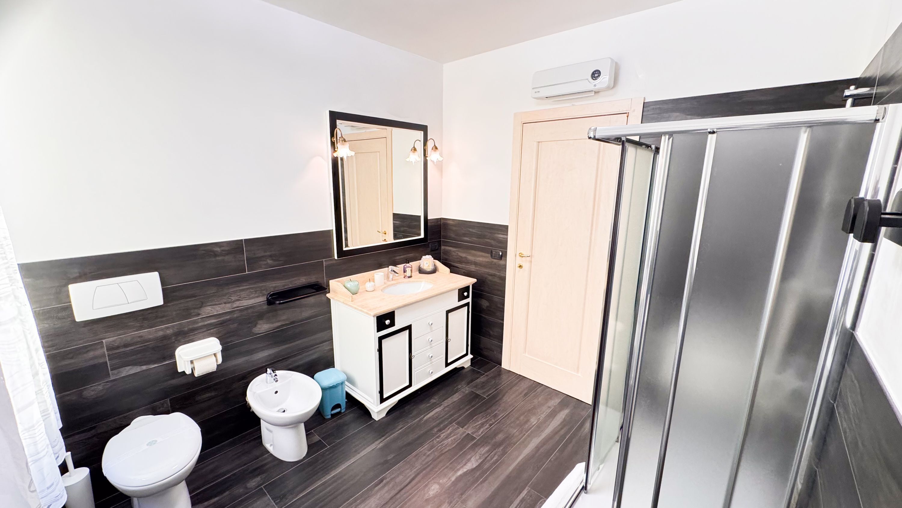 A bathroom with a white toilet, a sink with a mirror above it, a shower with a glass door, and dark wood flooring.