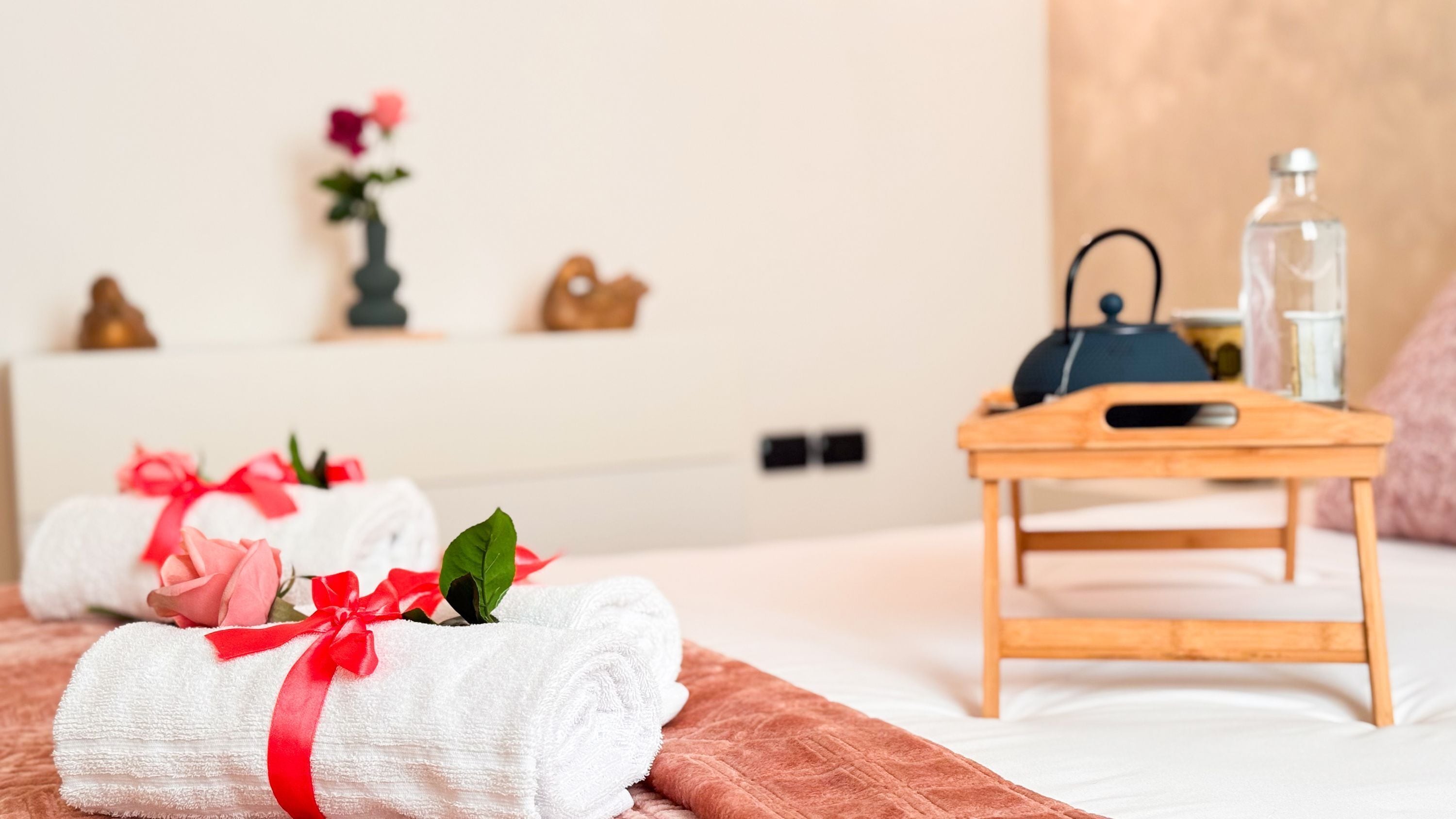 Een netjes ingerichte hotelkamer met een bed, een houten nachtkastje en een vaas met bloemen.
