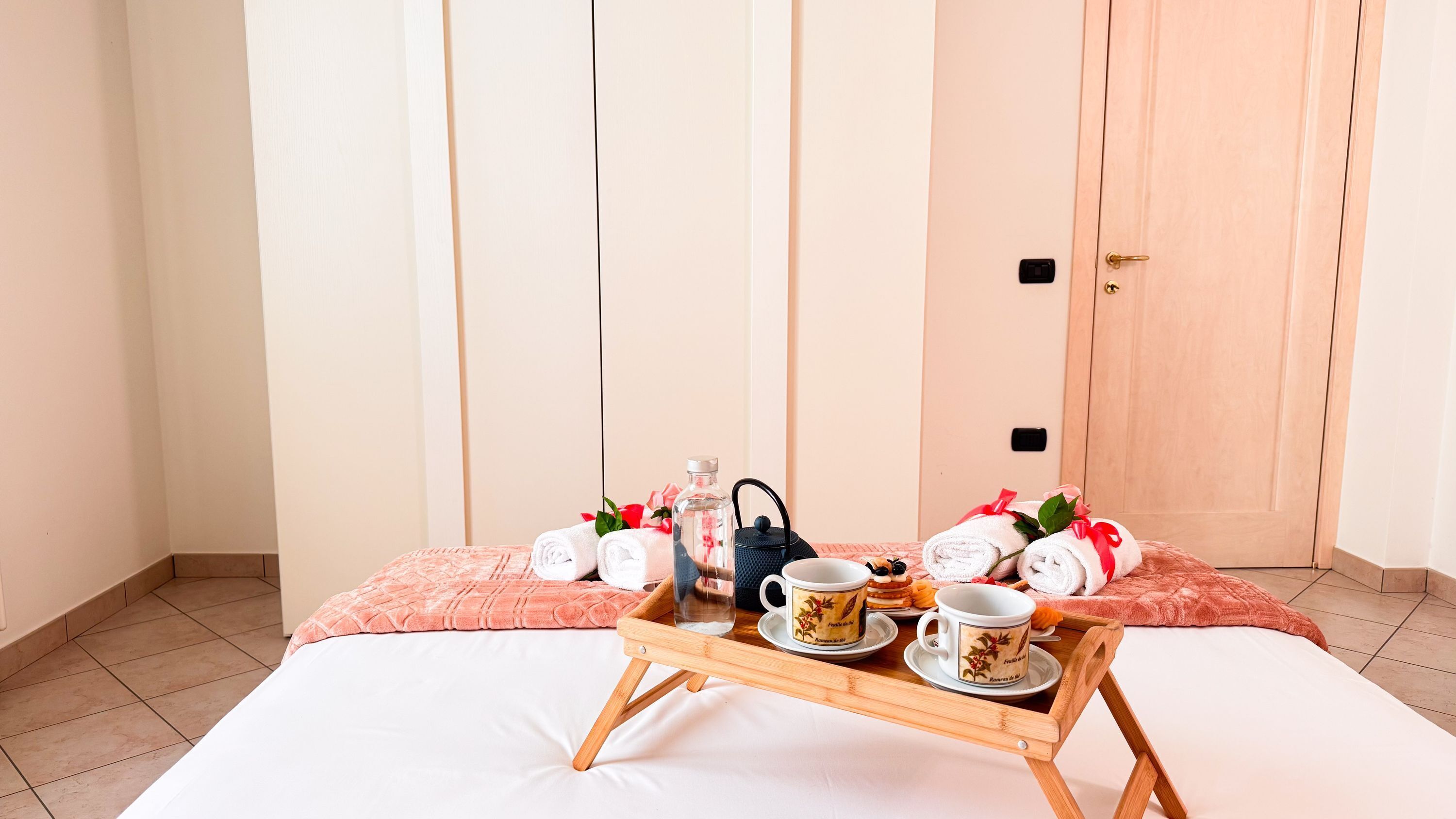 Een keurig opgemaakt bed met een dienblad met ontbijtartikelen, waaronder een mok, een fles en een kopje.