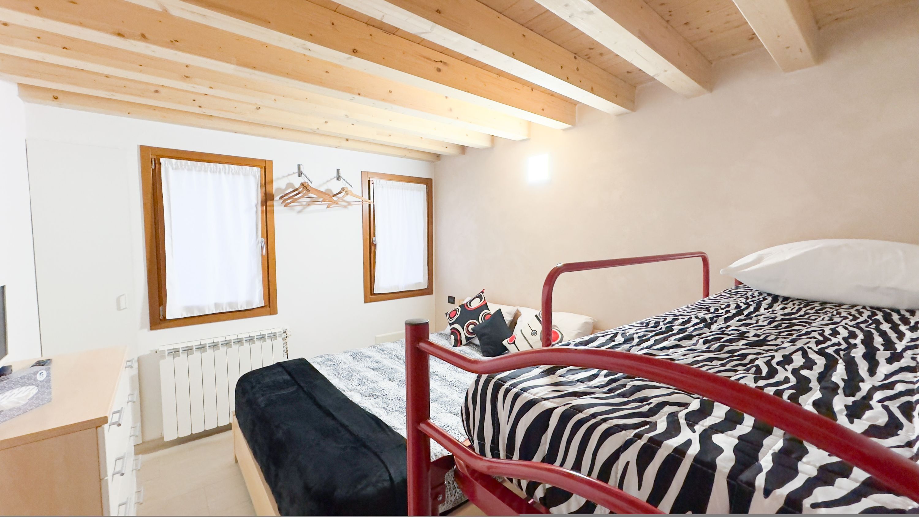 Un dormitorio con cama, radiador, ventana con cortinas y techo de madera.