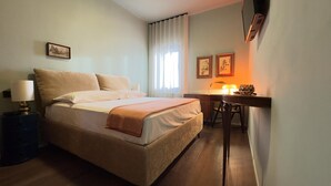 A neatly arranged hotel room with a bed, bedside table, lamp, and a desk with a chair.