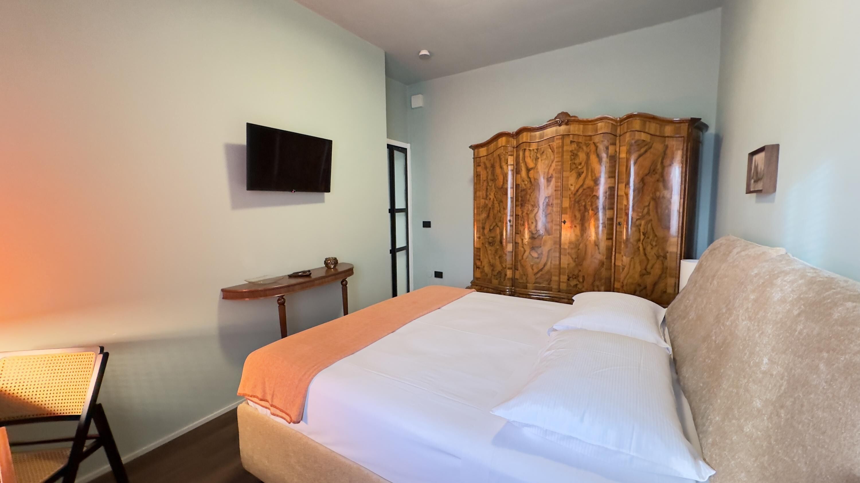 Un dormitorio con cama, un armario de madera, televisor montado en la pared y escritorio con silla.