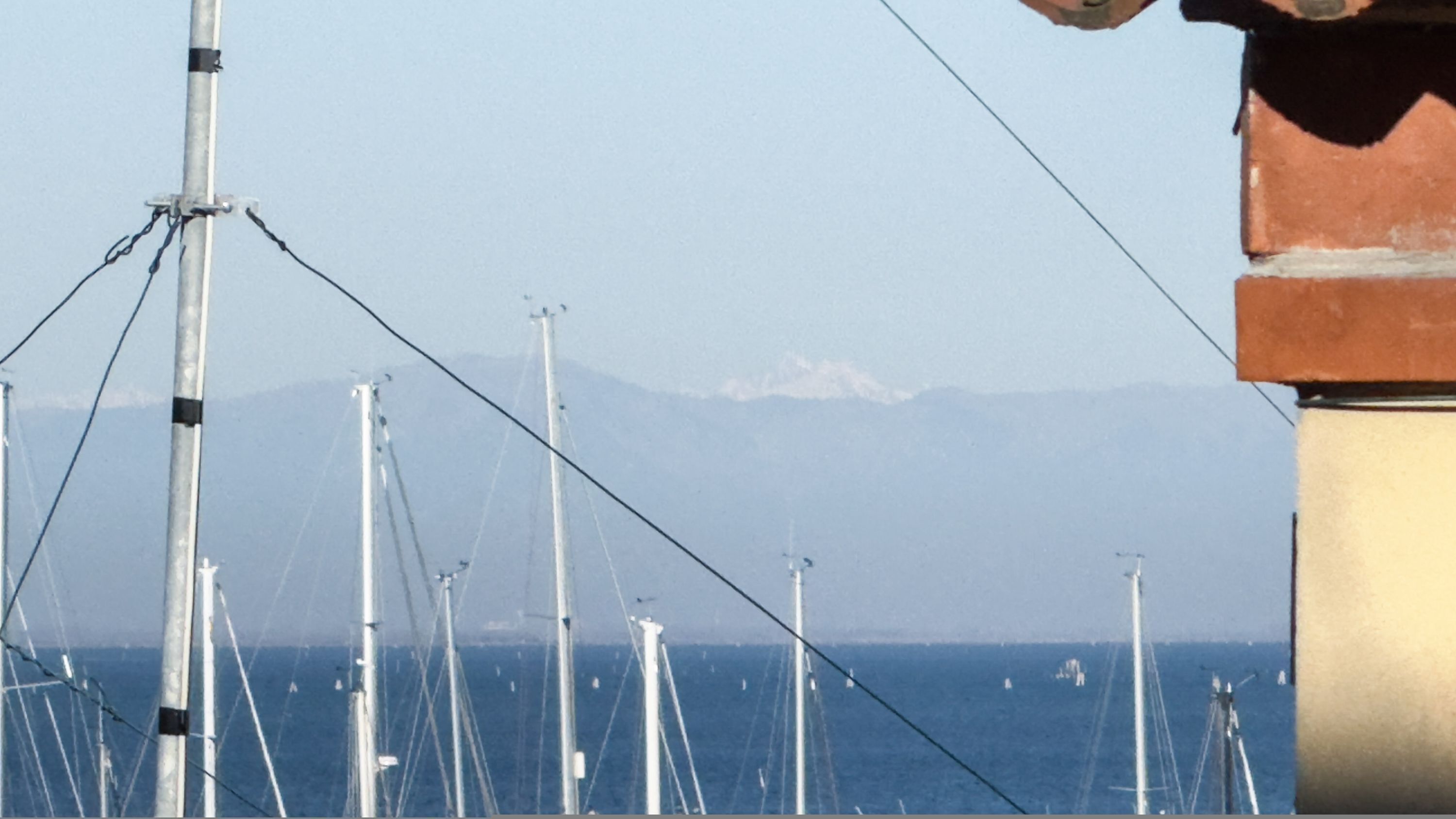 A coastal view with multiple tall structures, possibly communication towers, and a distant mountain range.