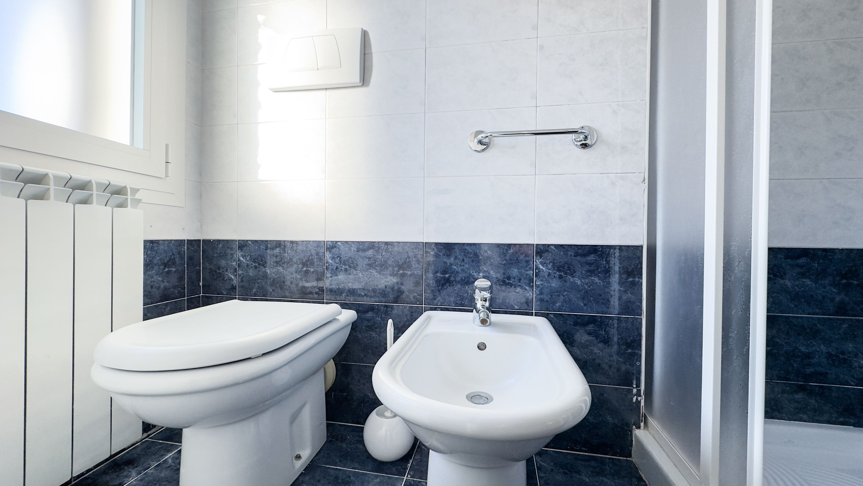 Ein Badezimmer mit Toilette, Bidet, gefliesten Wänden und einem Fenster.