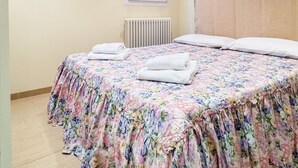 A bedroom with a floral bedspread, a radiator, and a window with patterned curtains. - Casa Dolce Casa by Ca-sa Check (Chioggia)