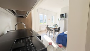 A compact kitchen with a modern faucet, a dining area with a table and chairs, and a blue sofa. - Onda Blu House by Ca-sa Check (Chioggia)