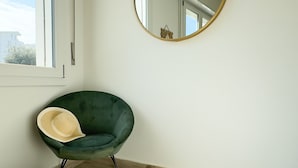 A room with a green chair, a yellow ottoman, a round mirror, and a window with a view of buildings. - Onda Blu House by Ca-sa Check (Chioggia)
