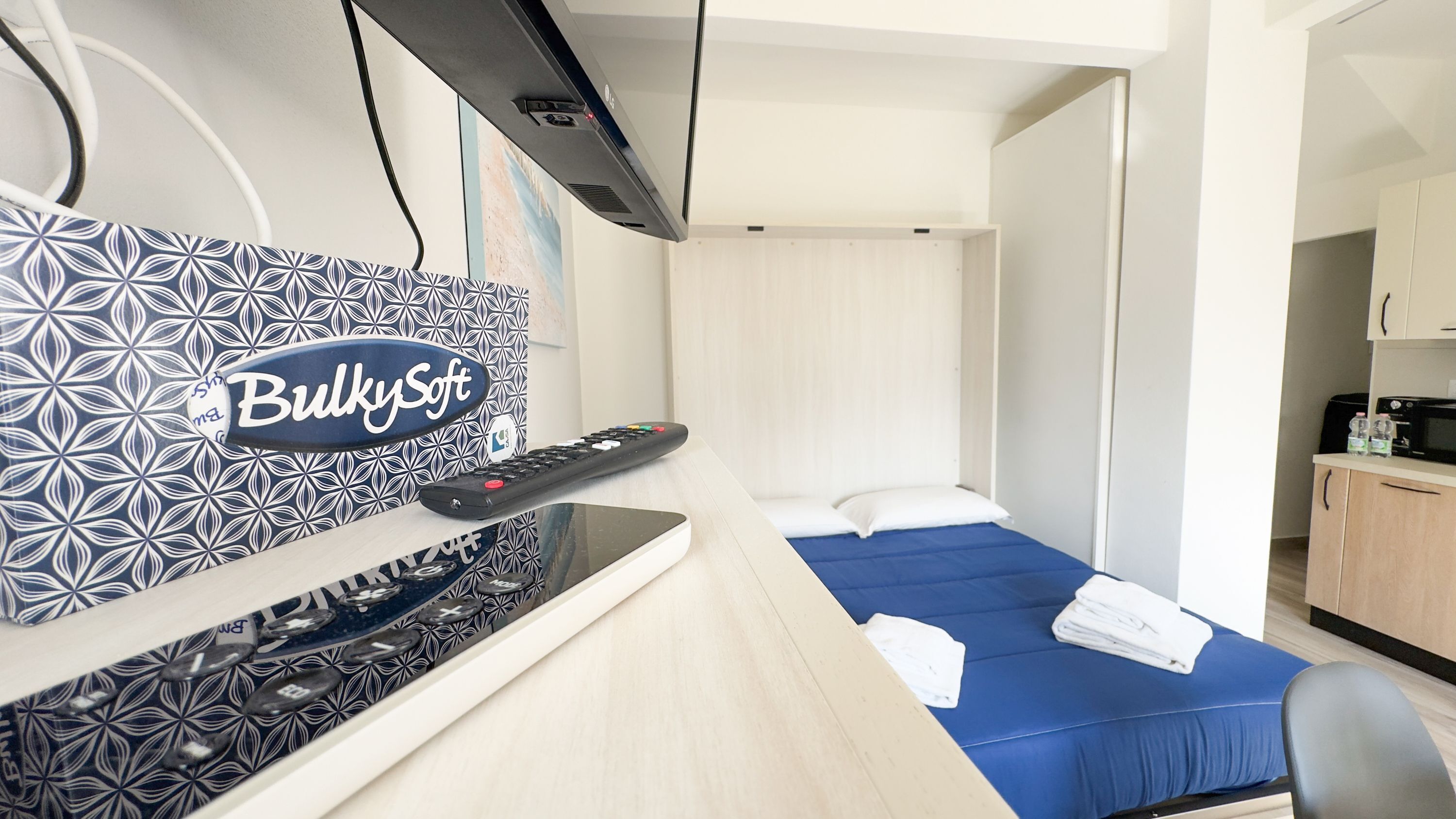 Een hotelkamer met een bed, een bureau met een computer en afstandsbediening, een magnetron en een kitchenette.