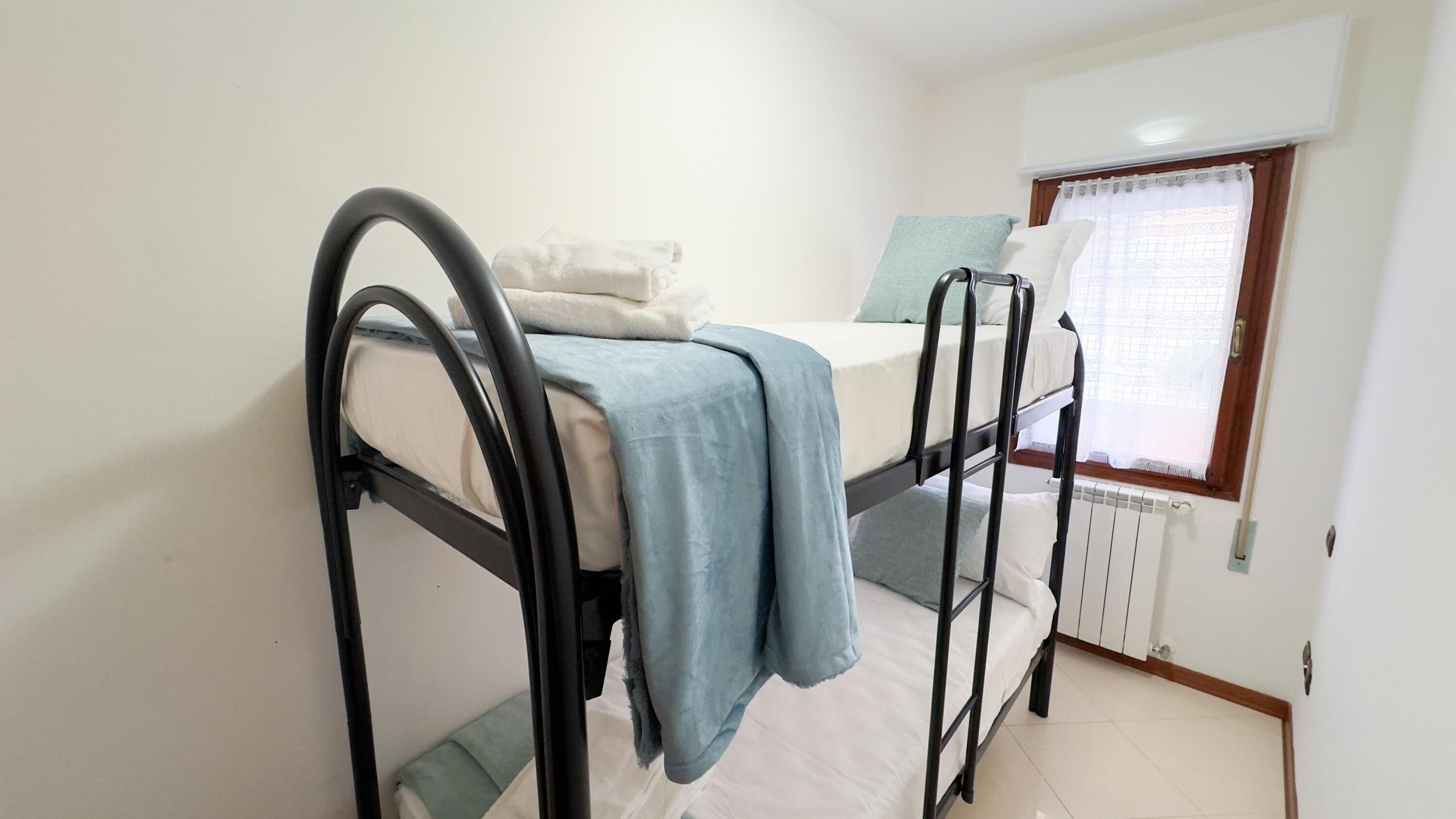 A bunk bed room with a window, white walls, and a radiator.