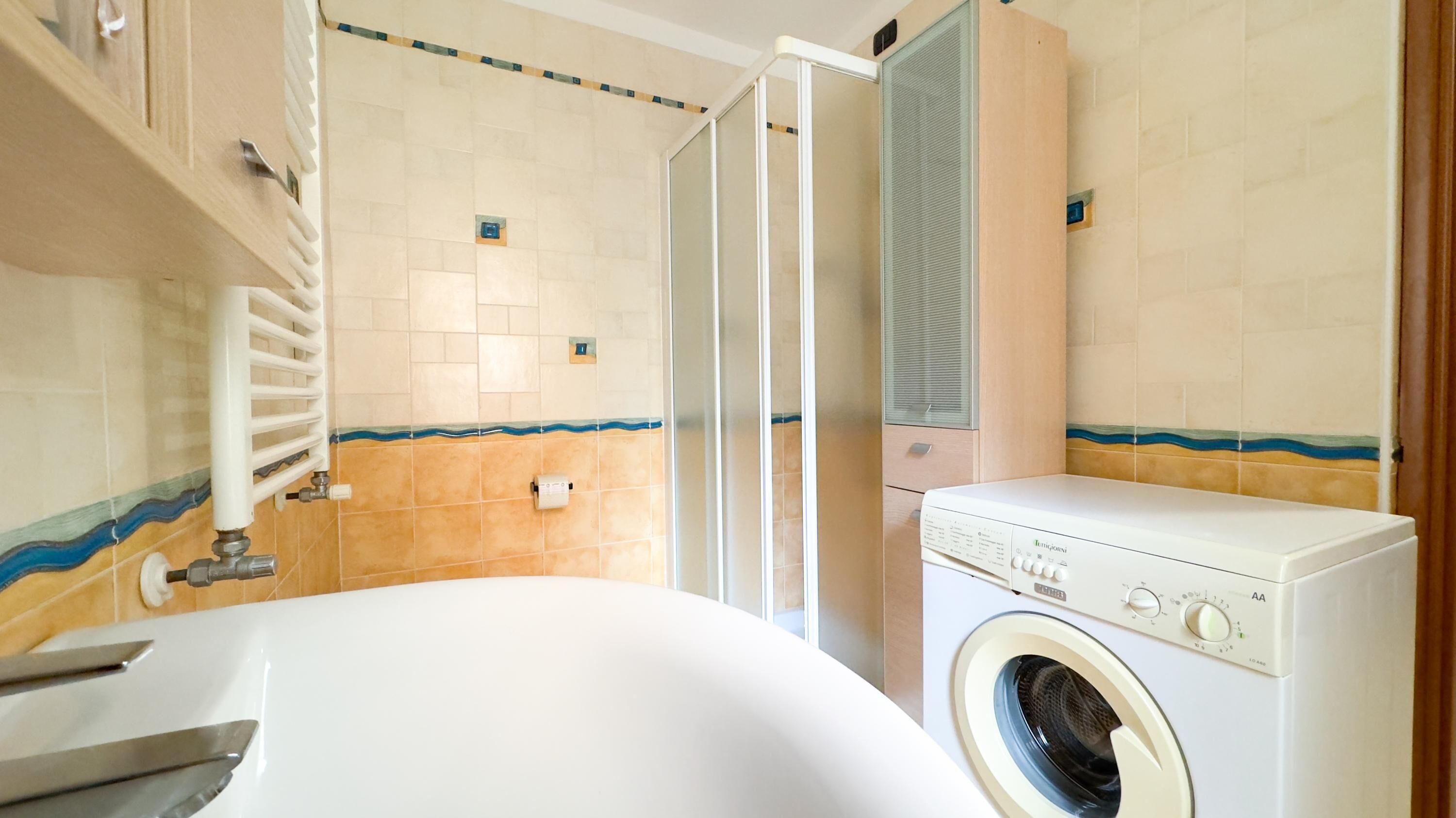 A compact bathroom with a white bathtub, a washing machine, and a shower area.