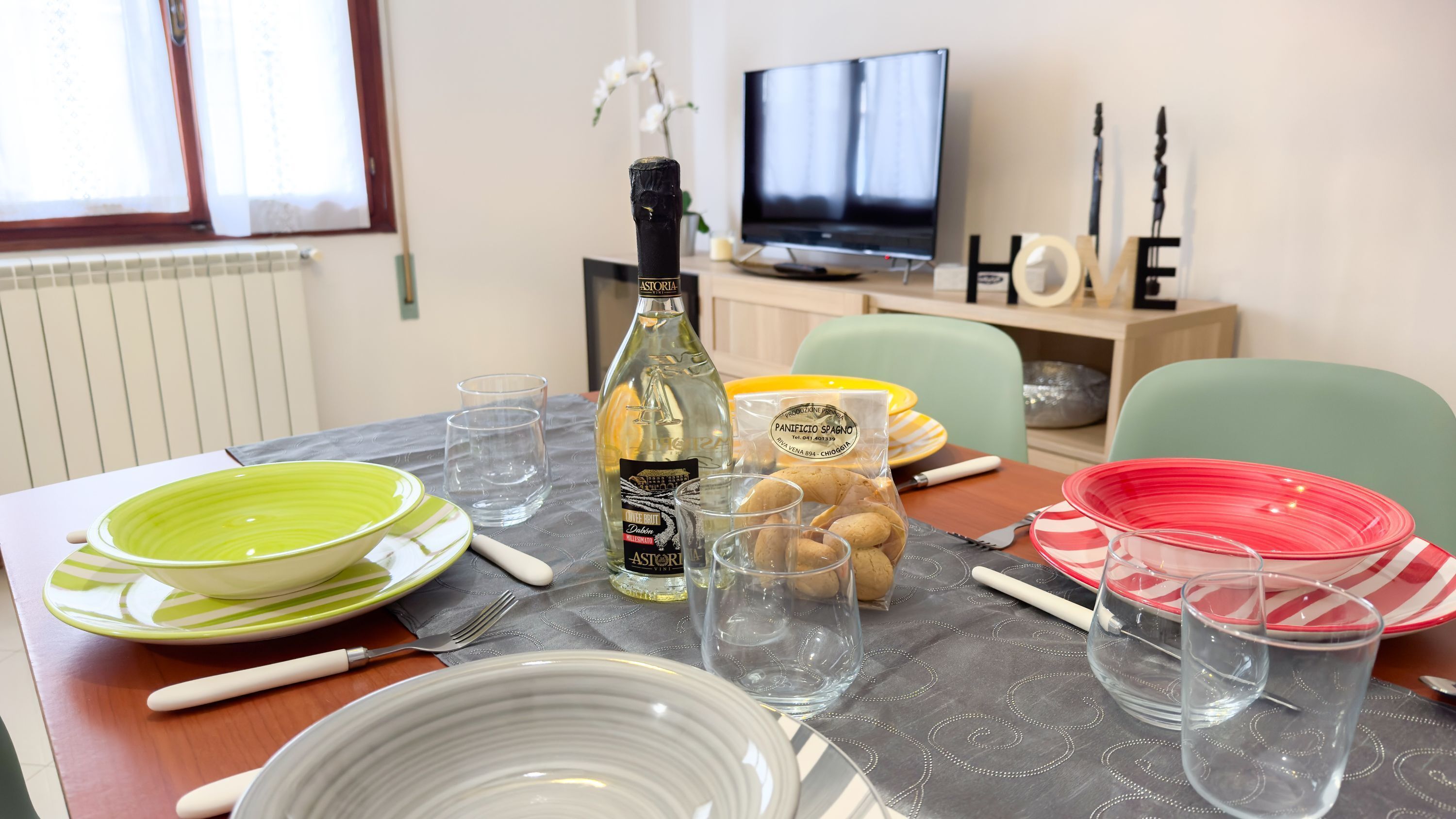A dining table set with plates, glasses, and a bottle of Astoria wine.