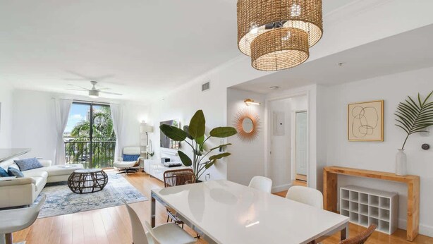 A modern living room with a dining area, white furniture, a large window, and a fireplace. - Palm Penthouse - Bright Designer Penthouse in the Heart of CityPlace (West Palm Beach)