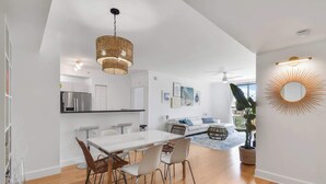 A modern kitchen with white cabinets, a stainless steel refrigerator, and a hanging wicker chandelier. - Palm Penthouse - Bright Designer Penthouse in the Heart of CityPlace (West Palm Beach)