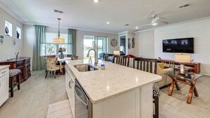 Uma cozinha moderna com uma ilha central, uma área de jantar com mesa de vidro e uma sala de estar com televisão de tela plana.