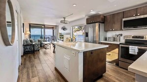 A modern kitchen with a central island, stainless steel appliances, and a view to the outside. - Remodeled 2 bedroom oceanfront condo, AC, 6 mile sandy beach, shaved ice, bakery (Kihei)