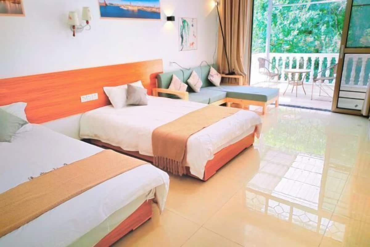 Ein Hotelzimmer mit zwei Betten, einem Sofa, einem kleinen Tisch und einem Balkon mit Blick auf Grünflächen.