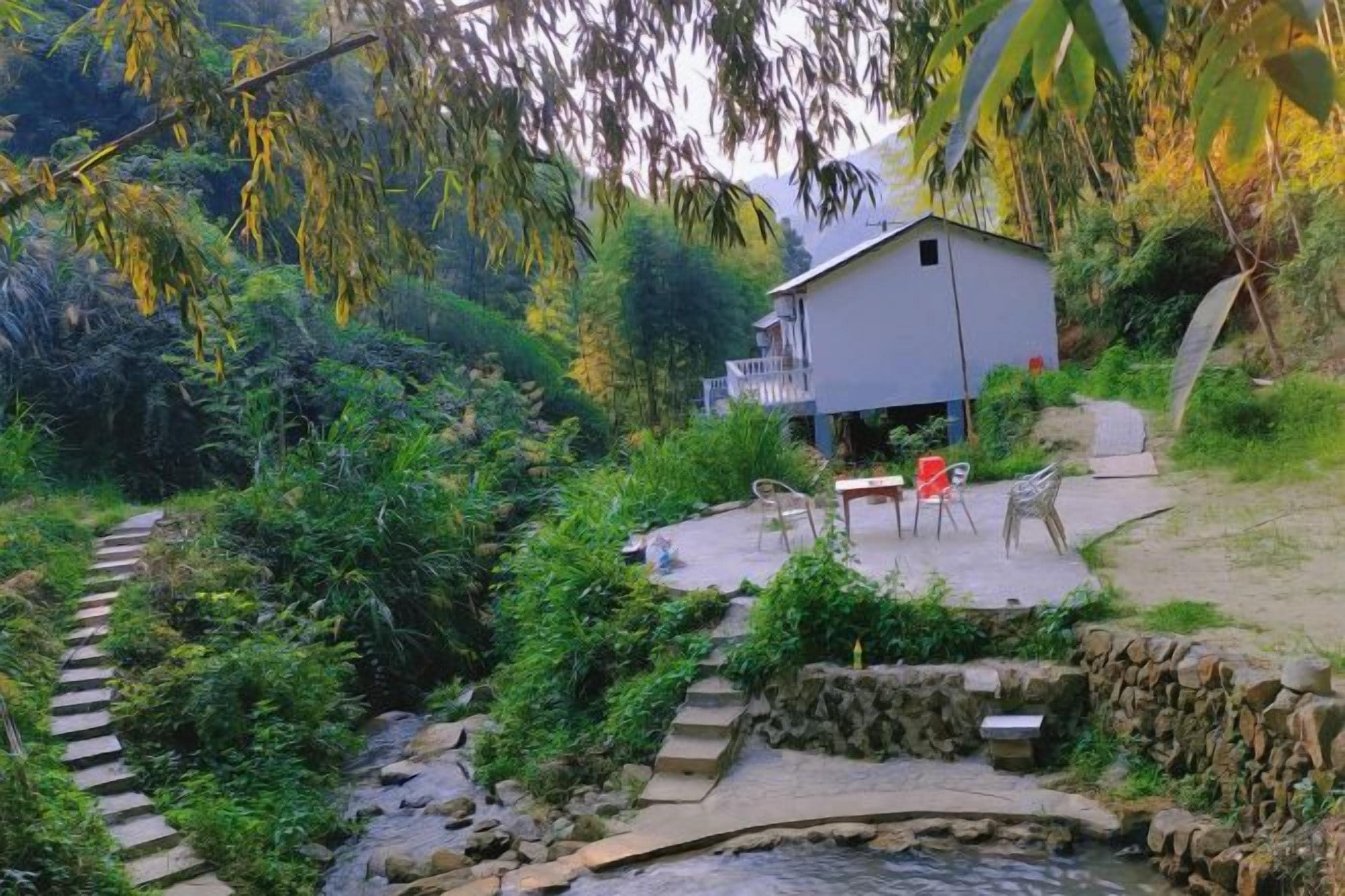 Eine rustikale Holzhütte mit einem Kiesweg, der zu einem kleinen Teich führt, umgeben von üppigem Grün.