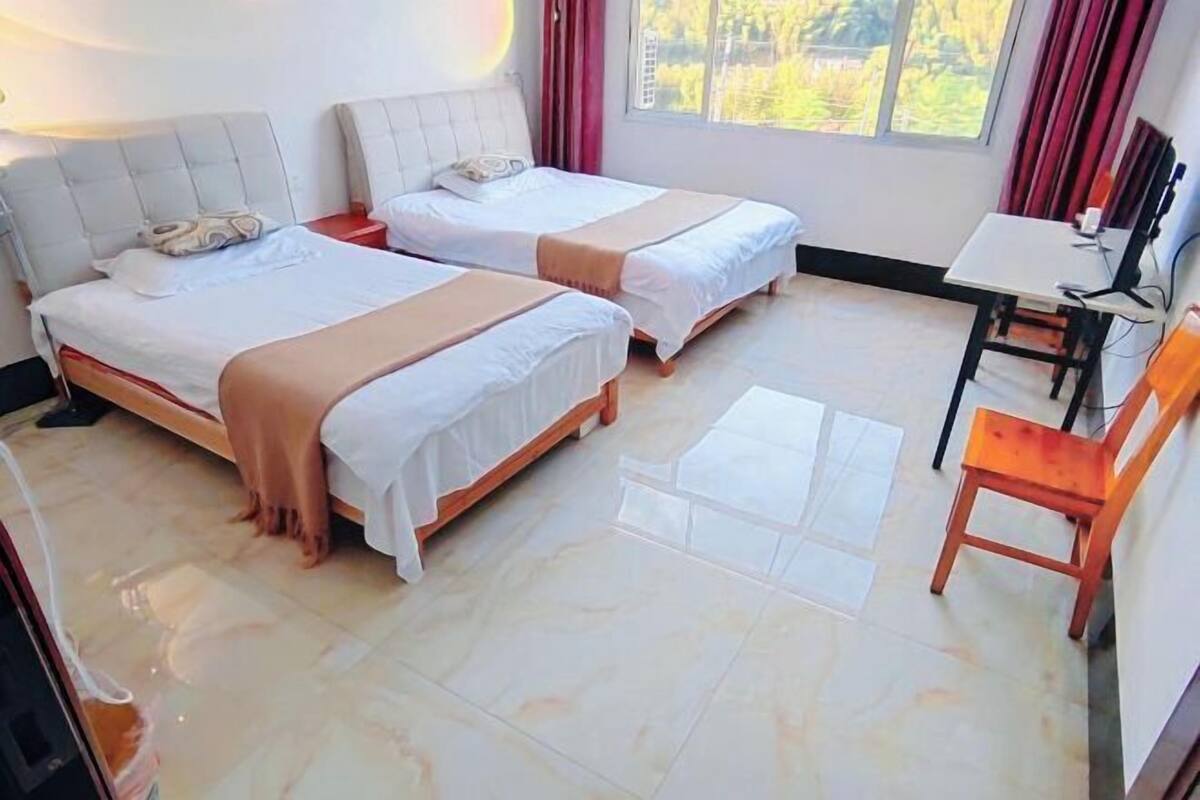 Ein Hotelzimmer mit zwei Betten, einem kleinen Tisch, einem Stuhl und einem Fenster mit Blick auf Grünflächen.