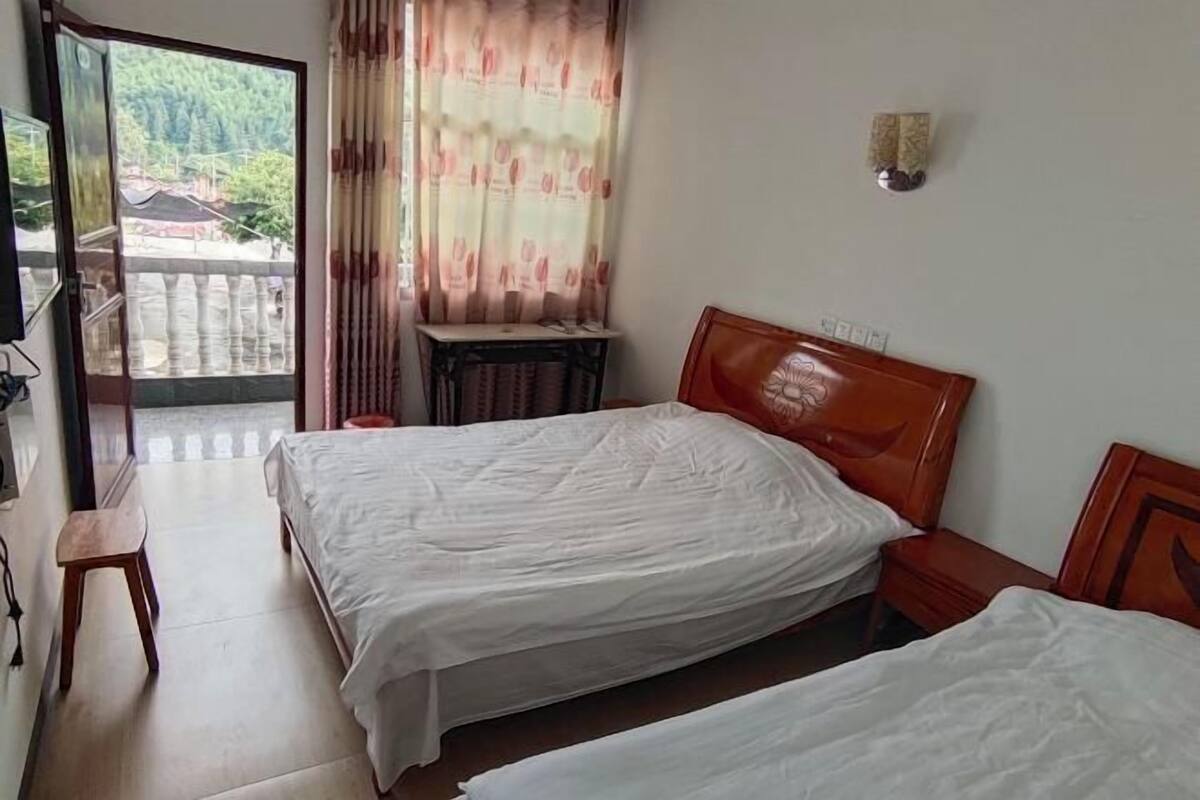 Ein Hotelzimmer mit zwei Betten, einem Schreibtisch und Blick auf einen Balkon.