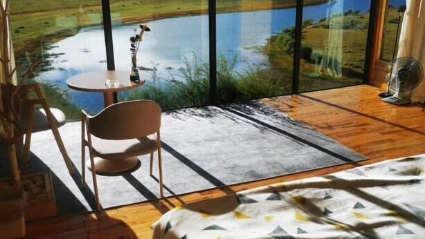 A bedroom with a large window overlooking a lake and fields, a bed, a chair, a small table, and a fan. - Shennong Valley Xishui Hotel (Yanling)