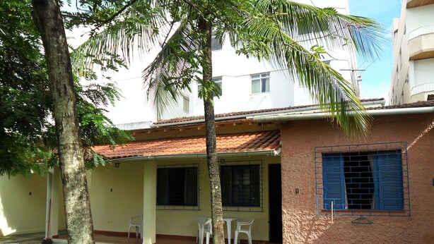 A residential building with a tiled roof, a small porch with plastic chairs, and a palm tree.