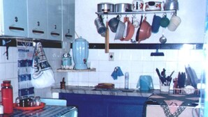 A compact kitchen with a blue countertop, a white chair, and a red kettle.