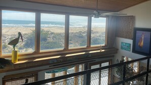 Ett rum med stora fönster med utsikt över en strand, en takfläkt och konstverk på väggarna.