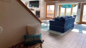 Ett vardagsrum med en blå soffa, en träbänk och en prydnadskudde med texten ”Välkommen till vårt hus vid stranden”.