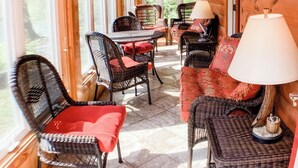 Une véranda aménagée avec des meubles en osier, un ventilateur de plafond et une vue sur l’extérieur.