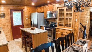 Une cuisine de style rustique, avec des éléments en bois, un îlot central, des appareils en acier inoxydable et un coin repas agrémenté d’une nappe à carreaux.