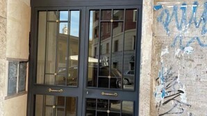 A black-framed glass door with a metal handle, set in a stone building with a visible number plate and a wall with graffiti. - Fefe's House (Roma)