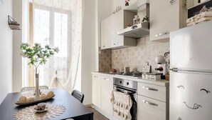 A modern kitchen with white cabinets, a stove, and a refrigerator. There is a dining table with a vase of flowers and a placemat. - Fefe's House (Roma)