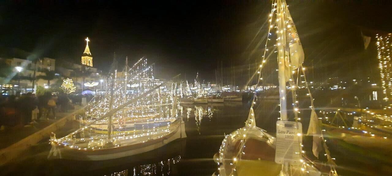 Uma marina à noite, com barcos iluminados e uma torre imponente ao fundo.