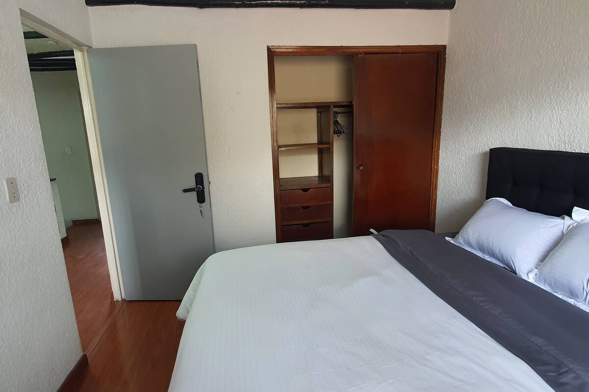 A bedroom with a bed, a wooden wardrobe, and a door leading to another room.