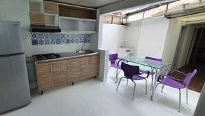 Eine kleine Küche mit Kühlschrank, Herd und violetten Stühlen um einem Glastisch.