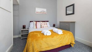 A hotel room with a bed, a nightstand, a dresser, a framed picture on the wall, and a mirror. - Large 4 Bedroom House Sleeps 9 With WiFi (Stockton-on-Tees)