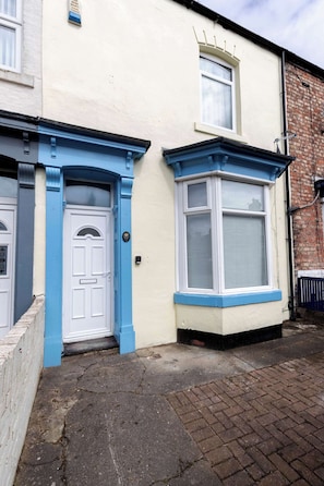 Une maison à deux étages, à l’extérieur blanc et bleu, avec une porte d’entrée et une fenêtre dotée de volets.