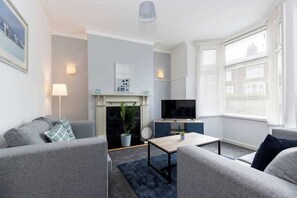 A modern living room with a fireplace, a television, and a large window with blinds. - Large 4 Bedroom House Sleeps 9 With WiFi (Stockton-on-Tees)