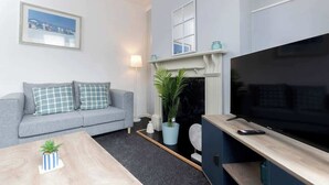 A modern living room with a grey sofa, a flat-screen TV, a fireplace, and a framed picture on the wall. - Large 4 Bedroom House Sleeps 9 With WiFi (Stockton-on-Tees)