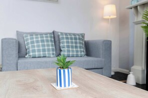 Un salon avec un canapé gris, un vase à rayures bleues et blanches et une table basse en bois.