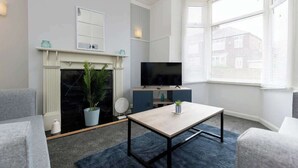 A modern living room with a fireplace, a flat-screen TV, and a dining table. - Large 4 Bedroom House Sleeps 9 With WiFi (Stockton-on-Tees)