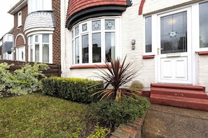 A residential building with a white facade, a bay window, and a red door.