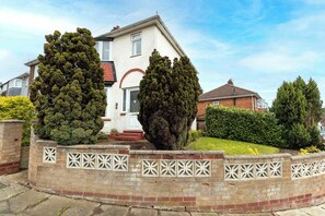 A residential house with a white facade, a brick chimney, and a well-maintained garden with trimmed hedges. - Comfortable 3 Bedroom Home Sleeps 5 (Stockton-on-Tees)