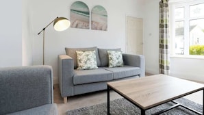 A modern living room with a grey sofa, a wooden coffee table, and a floor lamp. There are two wall-mounted paintings above the sofa. - Comfortable 3 Bedroom Home Sleeps 5 (Stockton-on-Tees)