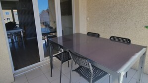 Une terrasse avec une table et des chaises en verre, une porte-fenêtre coulissante et une vue sur un bâtiment en arrière-plan.