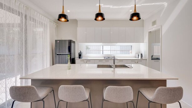 A modern kitchen with a large island, pendant lighting, and a view of the city.