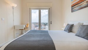 Ein Hotelzimmer mit Bett, Schreibtisch und Stuhl. Ein Balkon bietet Blick auf Gebäude.